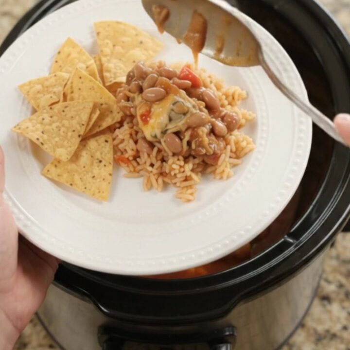 Slow cooker filled with chicken thighs in red enchilada sauce, topped with melted pepper jack and queso blanco