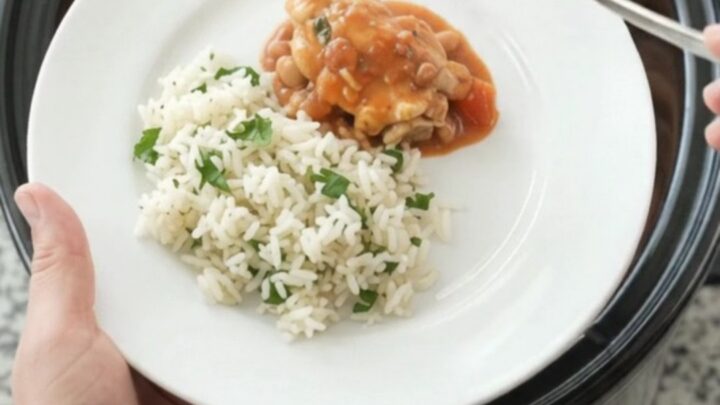 Slow cooker filled with creamy red enchilada chicken and pinto beans, topped with melted cheddar