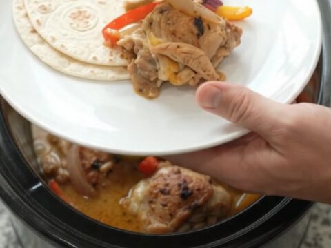 Slow cooker fajita chicken with creamy Monterey Jack sauce, bell peppers, and onions in a black crockpot.