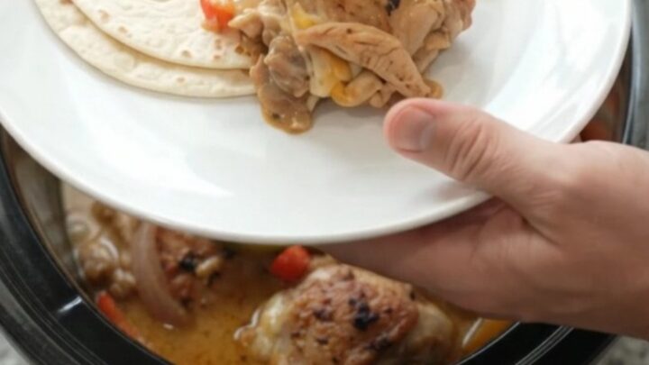 Slow cooker fajita chicken with creamy Monterey Jack sauce, bell peppers, and onions in a black crockpot.