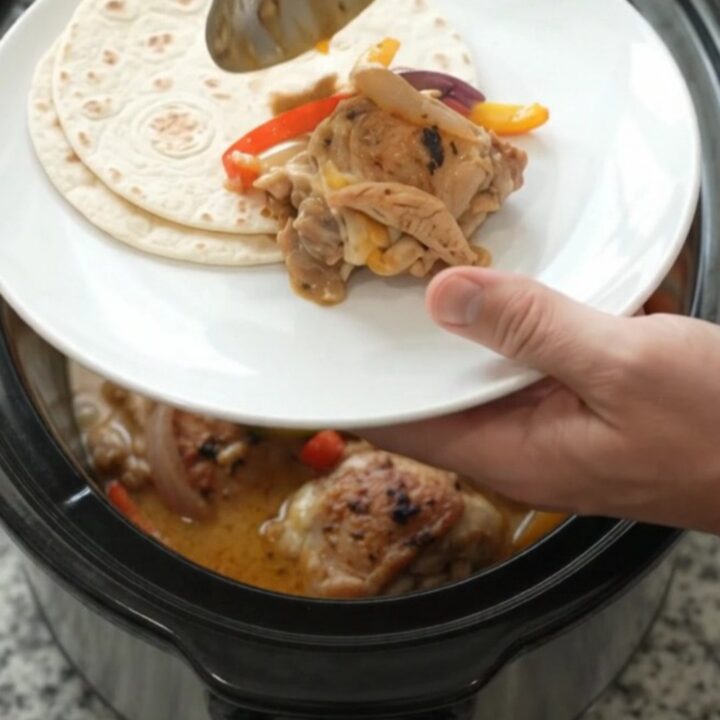 Slow cooker fajita chicken with creamy Monterey Jack sauce, bell peppers, and onions in a black crockpot.
