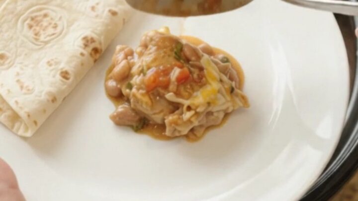 Slow cooker filled with shredded chicken in red enchilada sauce, pinto beans, and melted Monterey Jack cheese