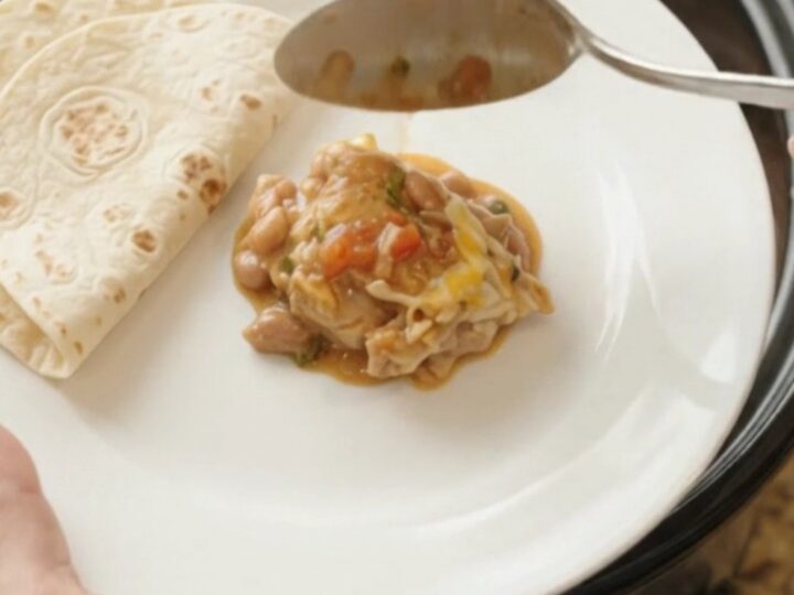 Slow cooker filled with shredded chicken in red enchilada sauce, pinto beans, and melted Monterey Jack cheese