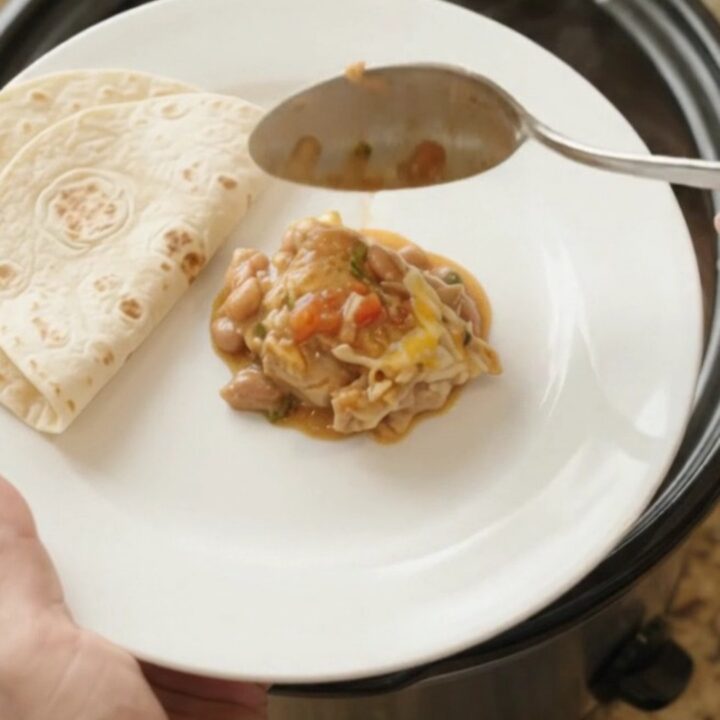 Slow cooker filled with shredded chicken in red enchilada sauce, pinto beans, and melted Monterey Jack cheese