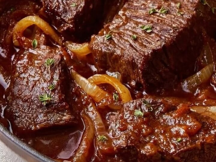 A close-up of tender beef short ribs in a Dutch oven, covered in a rich, glossy red wine and onion sauce.