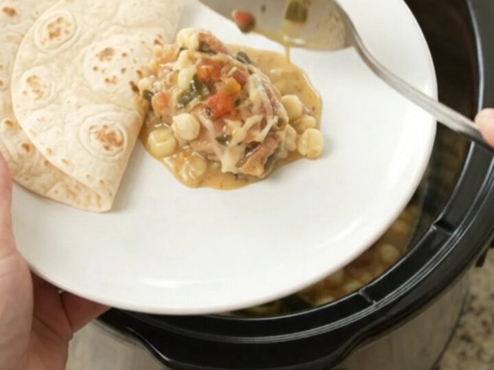 Creamy Crockpot chicken with poblanos and hominy in a black slow cooker, topped with melted cheese and salsa.