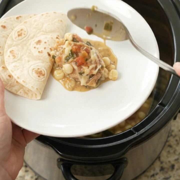 Creamy Crockpot chicken with poblanos and hominy in a black slow cooker, topped with melted cheese and salsa.
