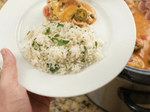 Slow cooker filled with creamy cheddar jalapeño chicken thighs, topped with melted cheese and tomatoes