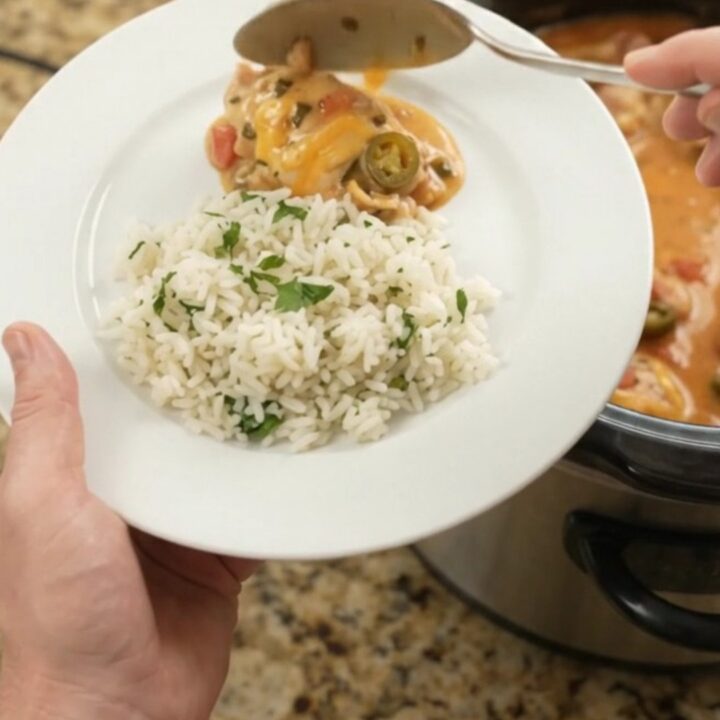 Slow cooker filled with creamy cheddar jalapeño chicken thighs, topped with melted cheese and tomatoes