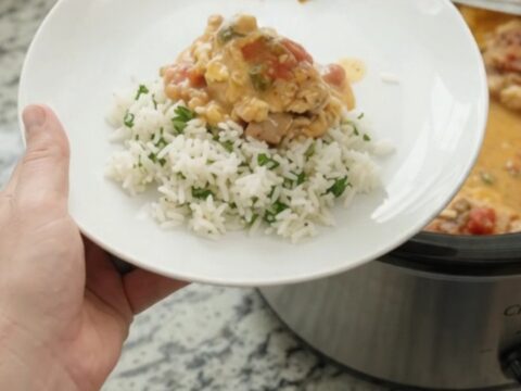 Slow cooker filled with creamy cheddar taco chicken, topped with melted cheese and salsa, with a spoon lifting a scoop.