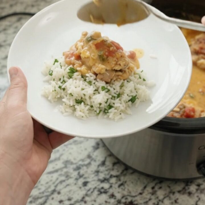 Slow cooker filled with creamy cheddar taco chicken, topped with melted cheese and salsa, with a spoon lifting a scoop.