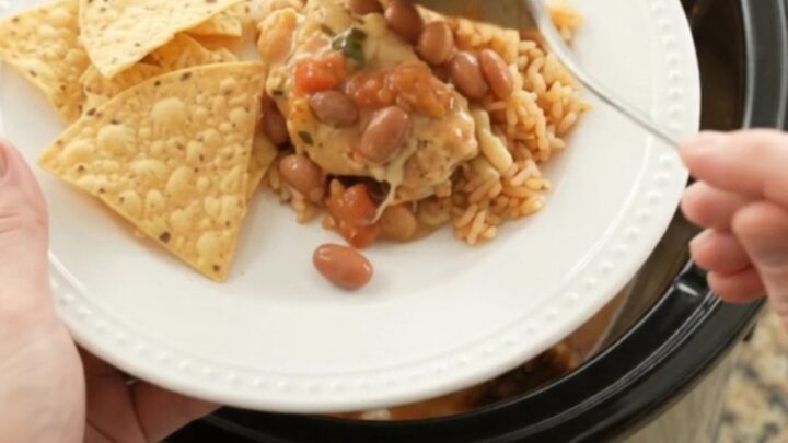 Slow cooker filled with shredded chicken, pinto beans, and melted cheese sauce, topped with a spoonful of the creamy mixture.