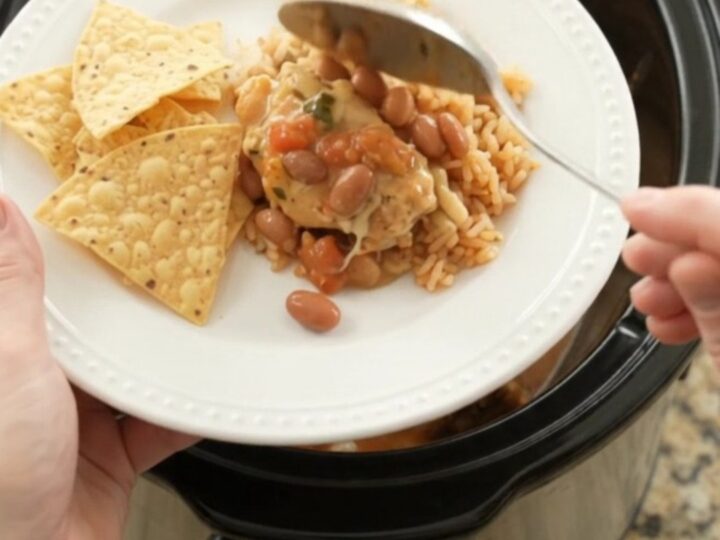 Slow cooker filled with shredded chicken, pinto beans, and melted cheese sauce, topped with a spoonful of the creamy mixture.