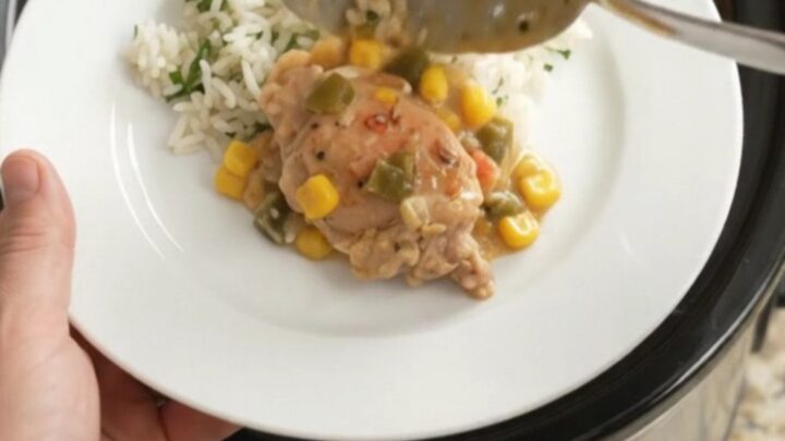 Creamy cheddar and green chile chicken thighs in a slow cooker, topped with melted cheese and corn.
