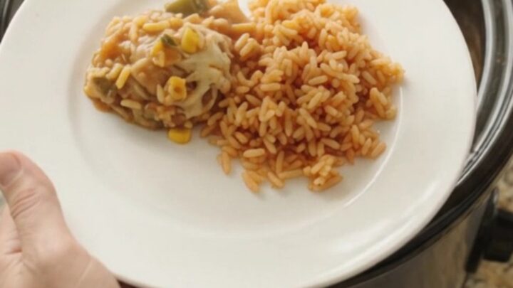 Slow cooker filled with tender chicken thighs in a creamy Oaxaca cheese sauce with green chiles and corn, steam rising.