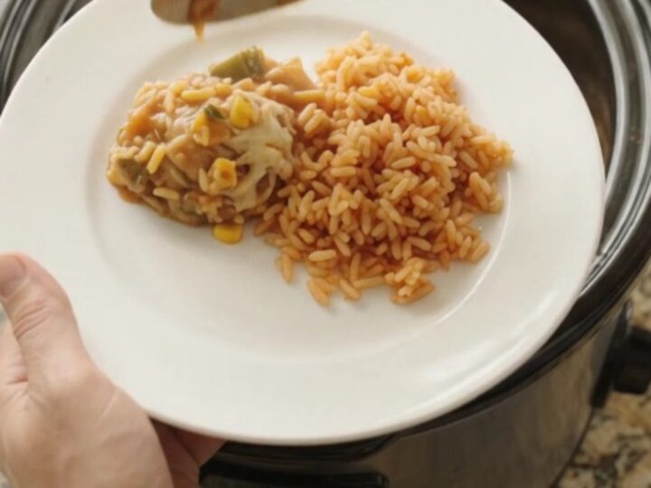 Slow cooker filled with tender chicken thighs in a creamy Oaxaca cheese sauce with green chiles and corn, steam rising.