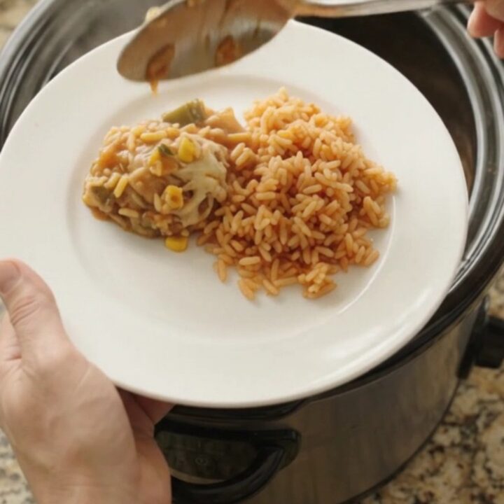 Slow cooker filled with tender chicken thighs in a creamy Oaxaca cheese sauce with green chiles and corn, steam rising.