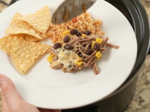 Slow cooker beef barbacoa with black beans and corn in a cheesy sauce, topped with melted pepper jack.