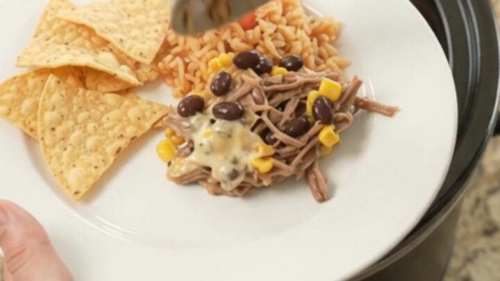 Slow cooker beef barbacoa with black beans and corn in a cheesy sauce, topped with melted pepper jack.