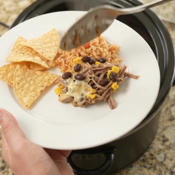 Slow cooker beef barbacoa with black beans and corn in a cheesy sauce, topped with melted pepper jack.