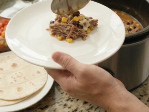 Slow cooker barbacoa with shredded beef, black beans, corn, and melted cheese in a black crockpot
