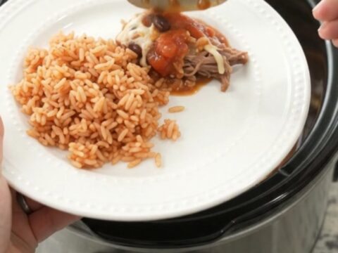 Slow cooker filled with shredded beef barbacoa, black beans, corn, and melted Oaxaca cheese, with steam rising.