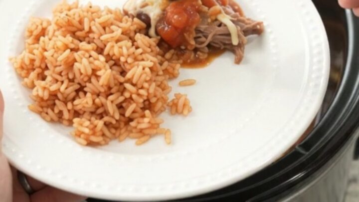 Slow cooker filled with shredded beef barbacoa, black beans, corn, and melted Oaxaca cheese, with steam rising.
