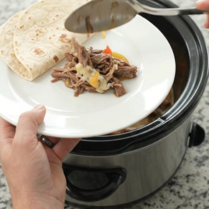 Slow cooker fajita beef barbacoa with melted Monterey Jack and peppers in a black Crockpot