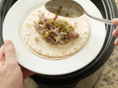 Shredded beef barbacoa in creamy salsa verde sauce in a slow cooker, topped with melted Monterey Jack cheese.