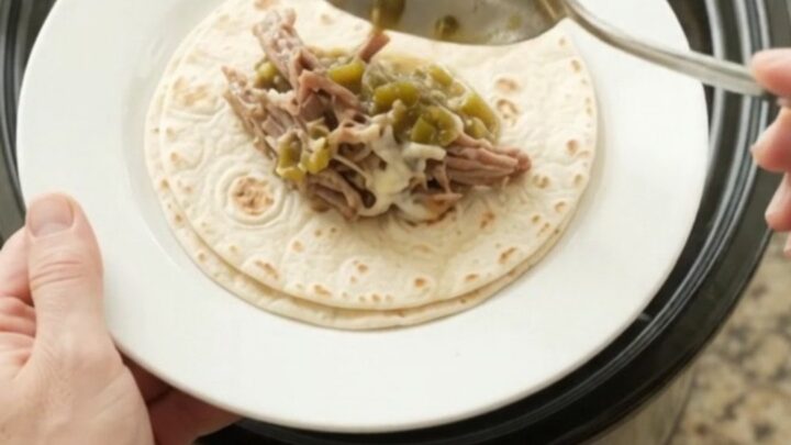 Shredded beef barbacoa in creamy salsa verde sauce in a slow cooker, topped with melted Monterey Jack cheese.