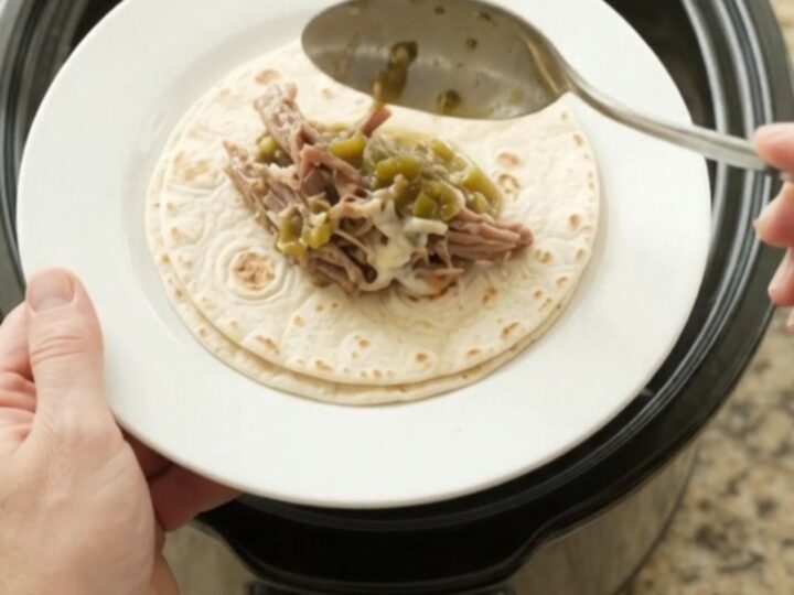 Shredded beef barbacoa in creamy salsa verde sauce in a slow cooker, topped with melted Monterey Jack cheese.
