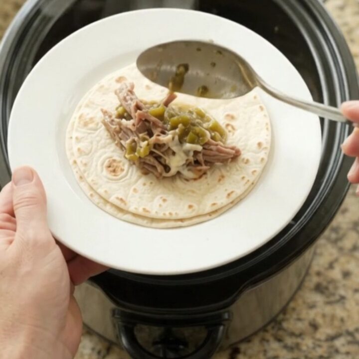 Shredded beef barbacoa in creamy salsa verde sauce in a slow cooker, topped with melted Monterey Jack cheese.