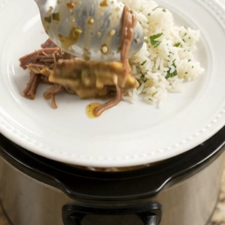 Shredded beef barbacoa in a slow cooker with creamy green sauce and melted cheddar
