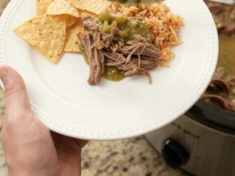A slow cooker filled with shredded beef barbacoa in a creamy green salsa and melted pepper jack cheese, with steam rising.