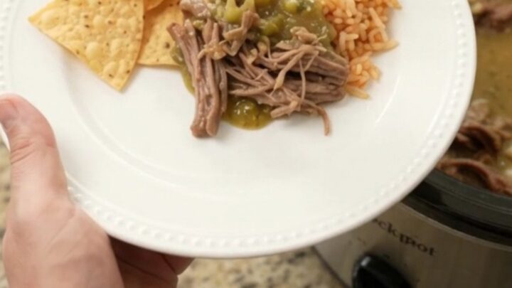 A slow cooker filled with shredded beef barbacoa in a creamy green salsa and melted pepper jack cheese, with steam rising.