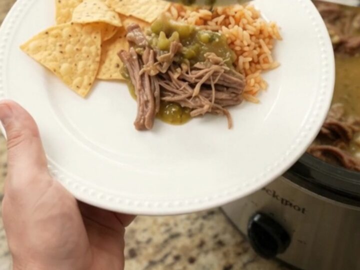 A slow cooker filled with shredded beef barbacoa in a creamy green salsa and melted pepper jack cheese, with steam rising.