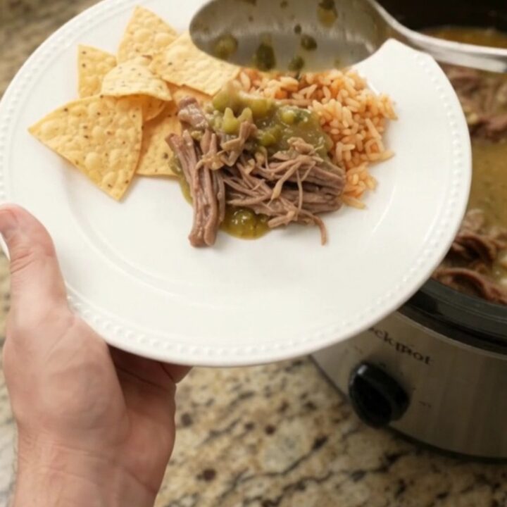 A slow cooker filled with shredded beef barbacoa in a creamy green salsa and melted pepper jack cheese, with steam rising.