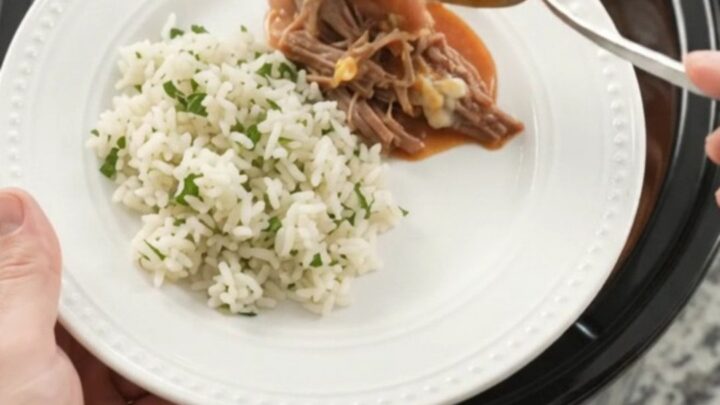 Slow cooker full of shredded beef barbacoa with red enchilada sauce and melted cheddar cheese