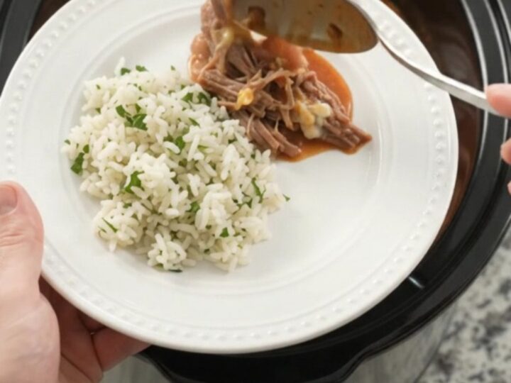 Slow cooker full of shredded beef barbacoa with red enchilada sauce and melted cheddar cheese