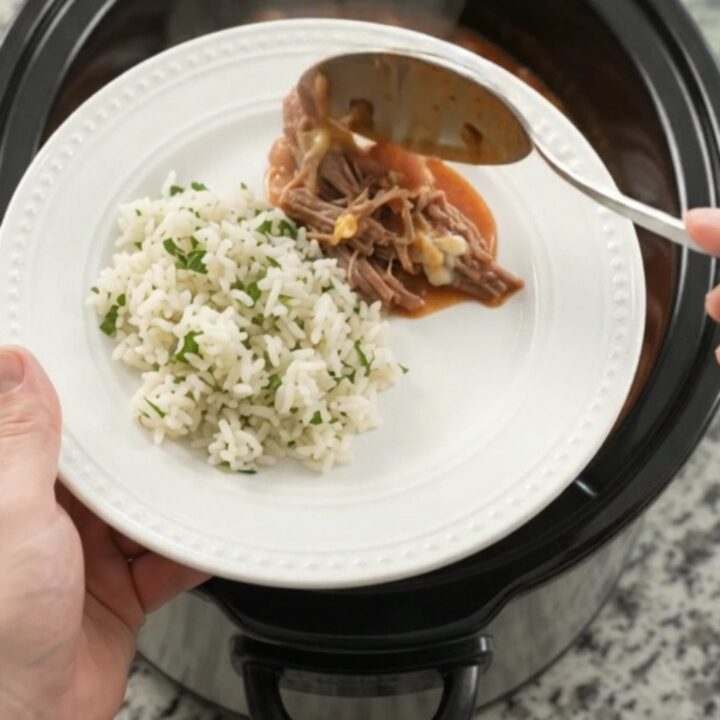 Slow cooker full of shredded beef barbacoa with red enchilada sauce and melted cheddar cheese