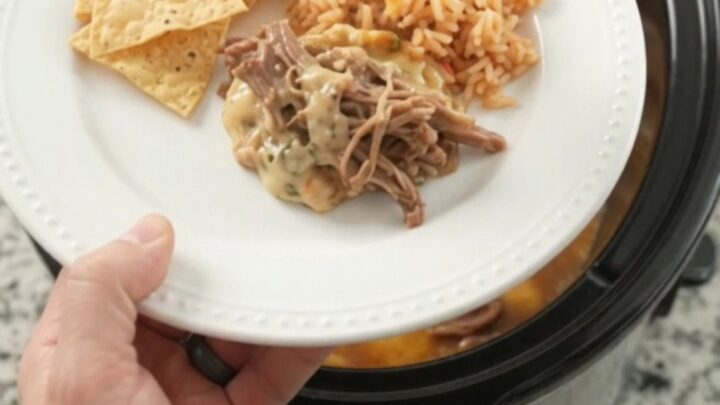 Slow cooker pepper jack chipotle pineapple beef barbacoa in a black crockpot with steam rising