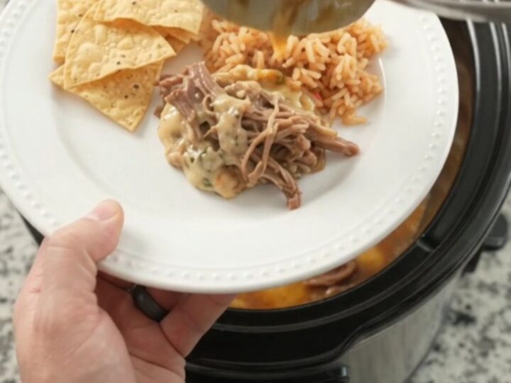 Slow cooker pepper jack chipotle pineapple beef barbacoa in a black crockpot with steam rising