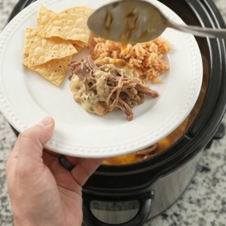 Slow cooker pepper jack chipotle pineapple beef barbacoa in a black crockpot with steam rising