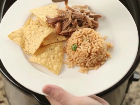 Slow cooker filled with shredded beef barbacoa in red sauce with pinto beans and melted cheese