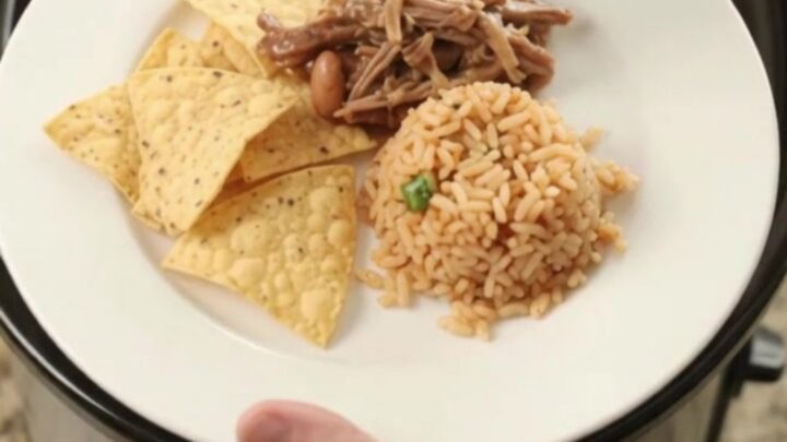 Slow cooker filled with shredded beef barbacoa in red sauce with pinto beans and melted cheese