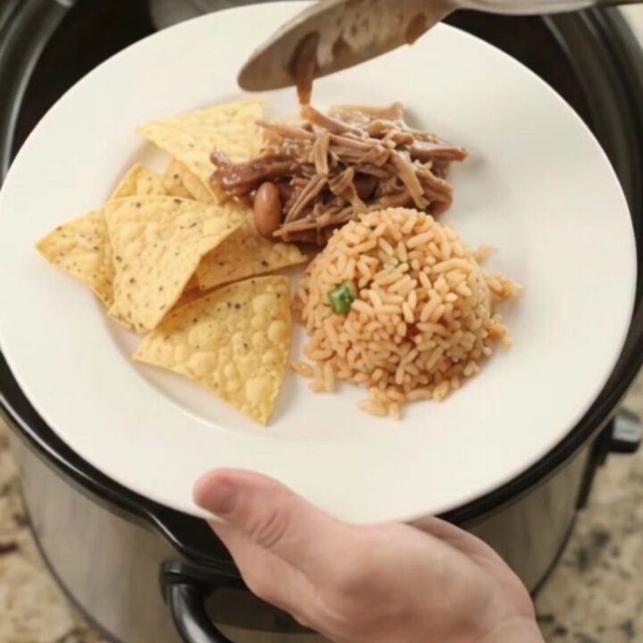 Slow cooker filled with shredded beef barbacoa in red sauce with pinto beans and melted cheese