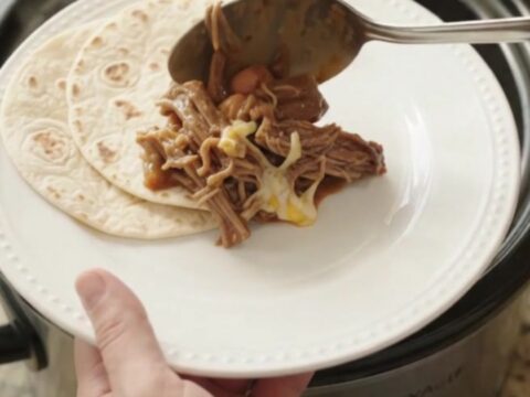 Slow cooker red enchilada beef barbacoa with melted cheese and pinto beans in a crockpot