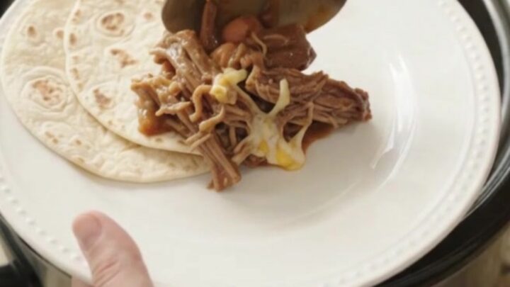 Slow cooker red enchilada beef barbacoa with melted cheese and pinto beans in a crockpot