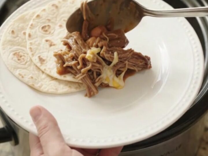 Slow cooker red enchilada beef barbacoa with melted cheese and pinto beans in a crockpot