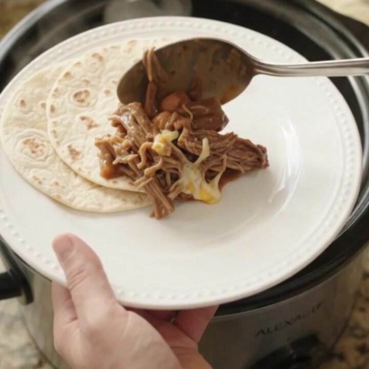 Slow cooker red enchilada beef barbacoa with melted cheese and pinto beans in a crockpot